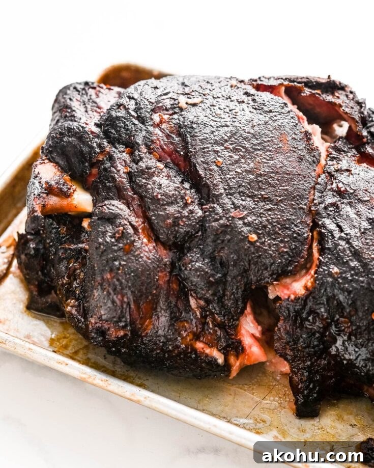 A smoked pork butt resting on a rimmed baking sheet before pulling the meat.