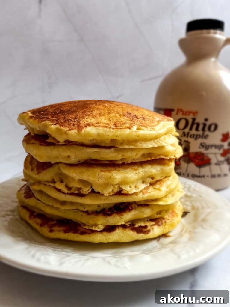 a stack of cooked pancakes and a jug of maple syrup.