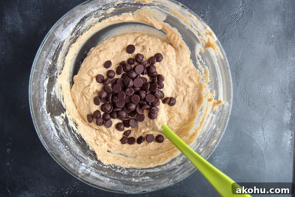 Moist Banana Bread with Chocolate Chips: Classic Recipe 4 batter with chocolate chips and a green rubber spatula in a bowl.