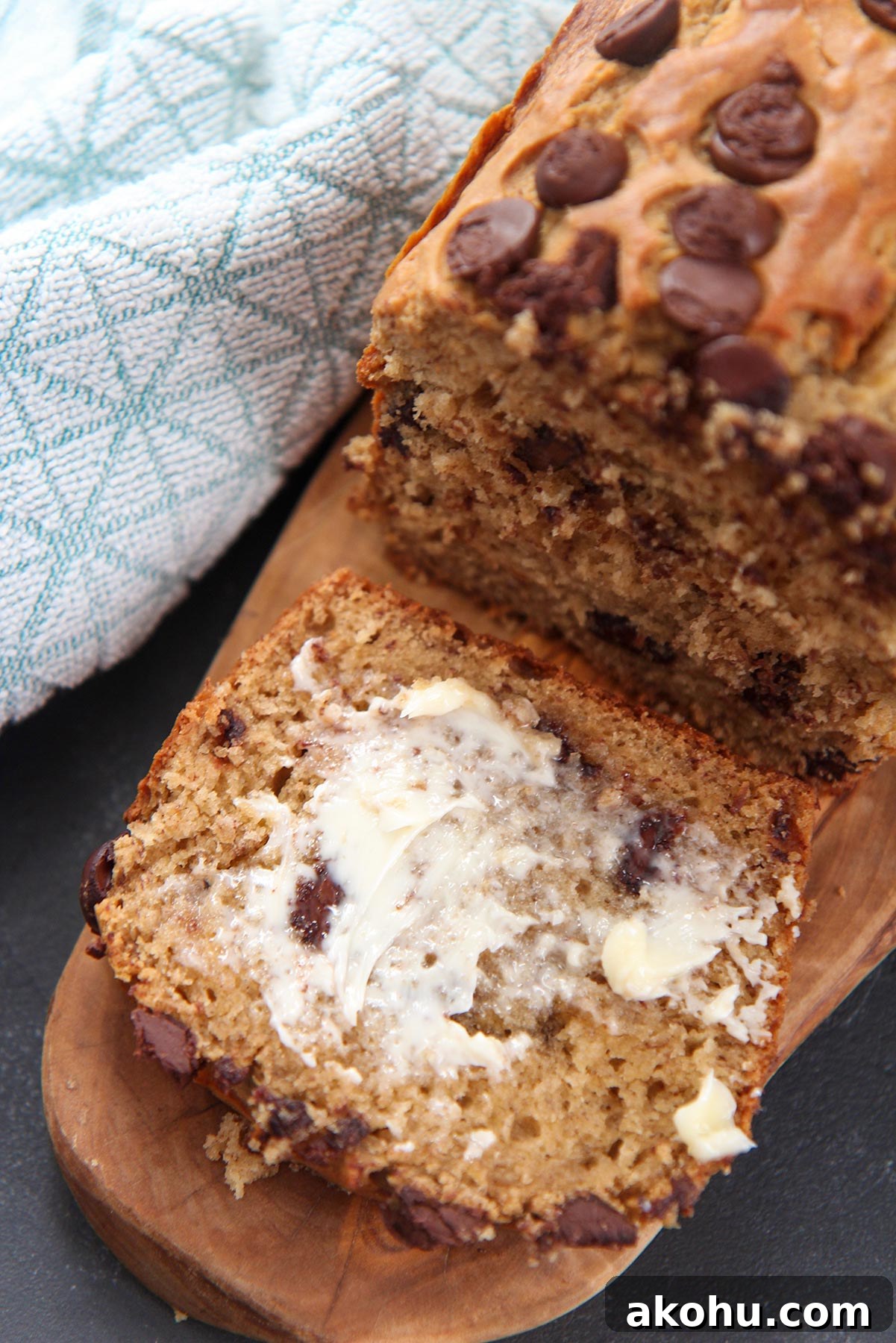 Moist Banana Bread with Chocolate Chips: Classic Recipe 6 a slice of bread with butter smeared on top. A blue towel on the side.