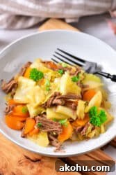 Plate of corned beef with a cabbage stew twist, complemented by carrots and garnished with parsley, all elegantly presented on a wooden surface.