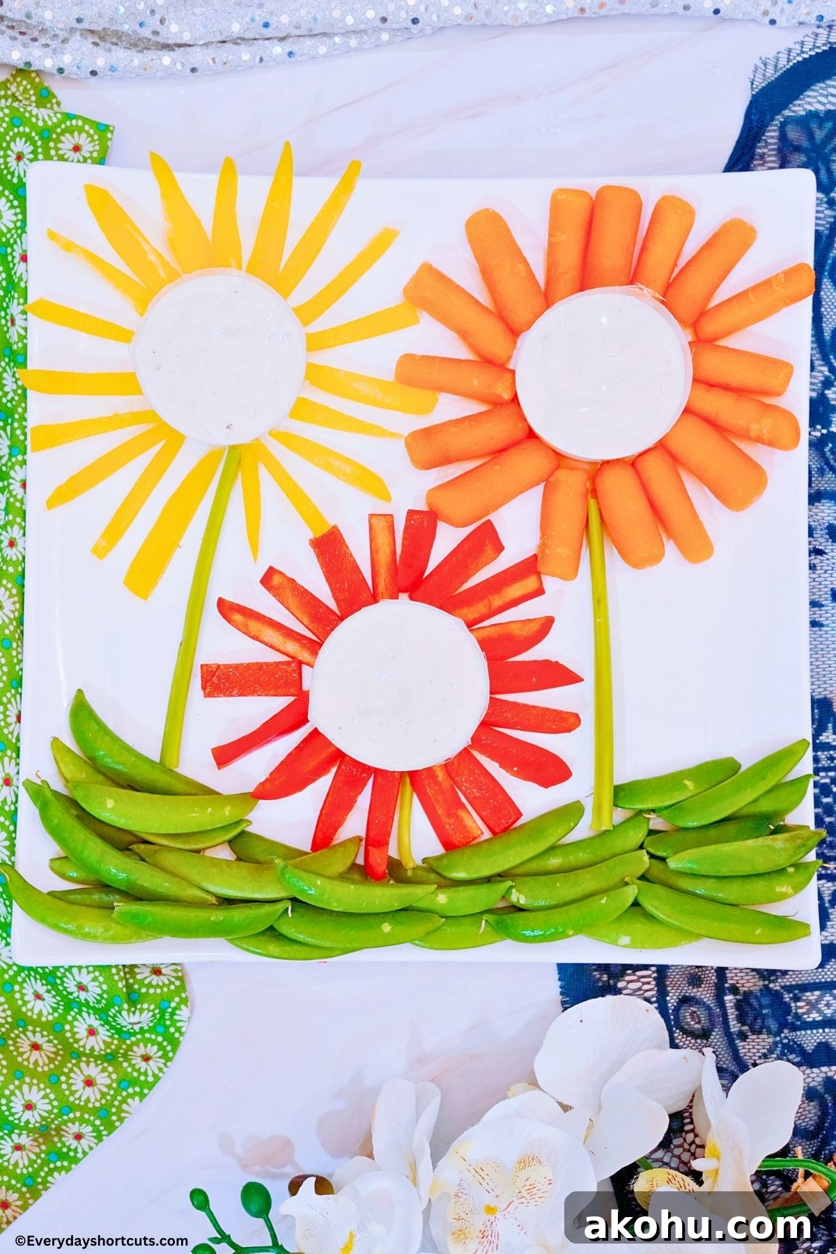 Blooming Vegetable Platter: Stunning Veggie Flower Tray Tutorial 2 carrots red and yellow bell peppers in the shape of flowers with bowls of ranch dressing in the middle of each one celery sticks for stems and snap peas for grass on a platter