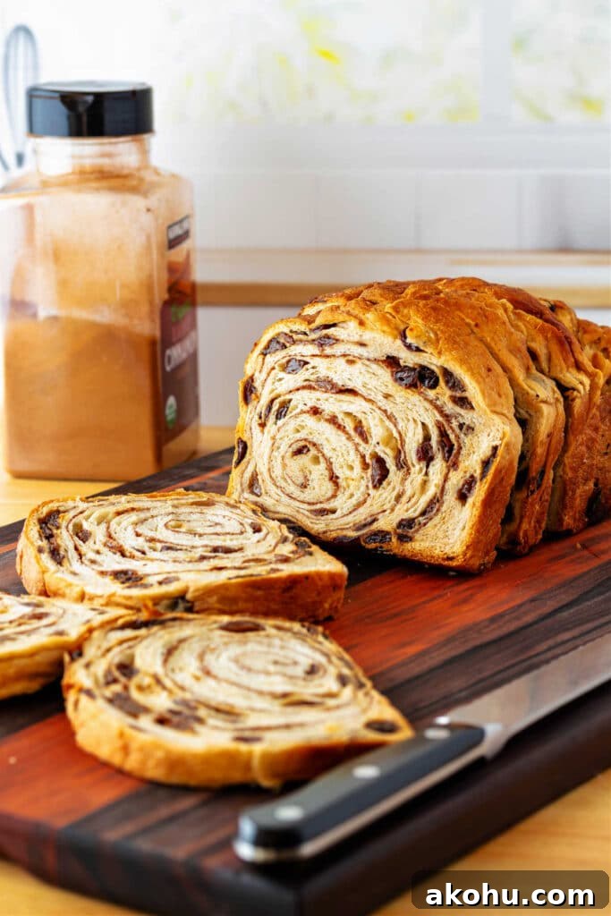Why Cinnamon Swirl Bread Splits During Baking — How to Prevent It 2 A sliced loaf of cinnamon raisin bread on a cutting board with a bread knife and a jar of ground cinnamon in the background.
