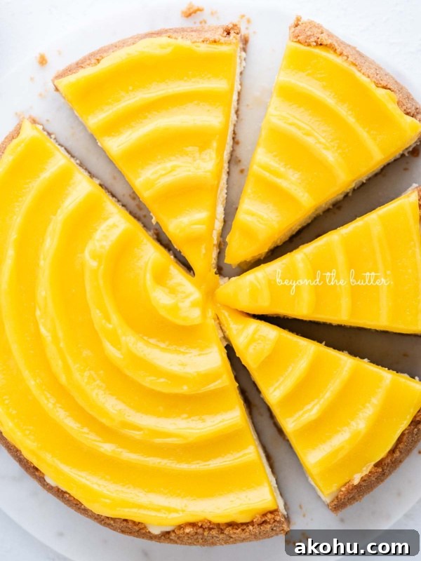 Lemon cheesecake topped with lemon curd cut into slices on a marble cake plate with white background.