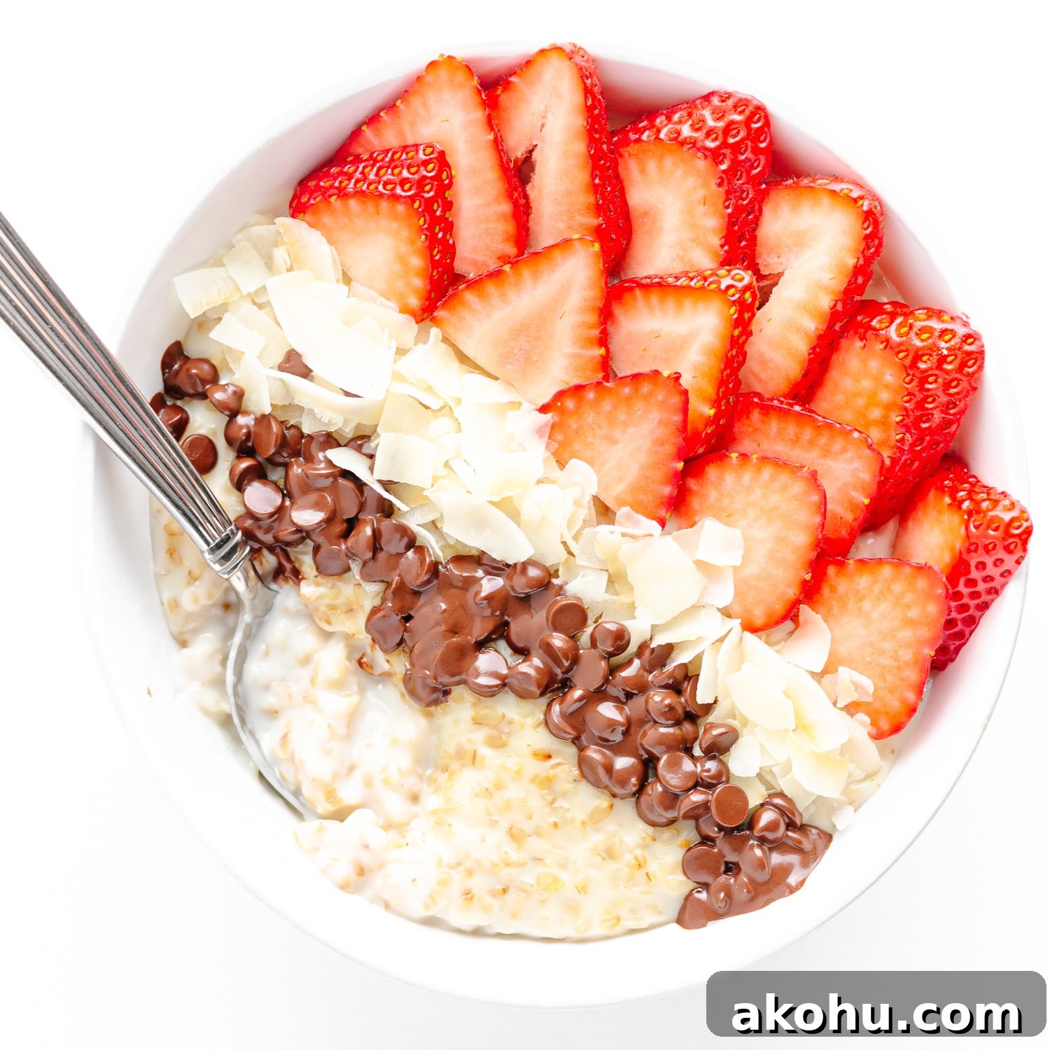 Bowl of creamy steel cut oats topped with sliced strawberries, coconut flakes and mini chocolate chips.