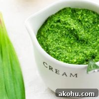ramp pesto in a small pitcher with ramp leaves, a lemon, and pine nuts