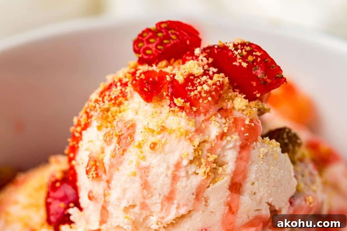 Close-up of a bowl of ice cream topped with crushed cookies, strawberry pieces, and a drizzle of strawberry sauce.