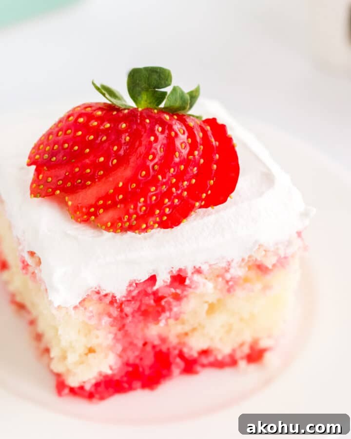 a square slice of white cake with strawberry filling on a white place topped with a strawberry