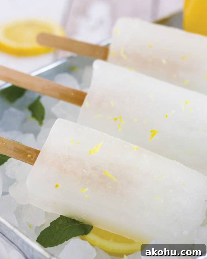 Three lemonade popsicles lying on ice with lemon slices and fresh mint.
