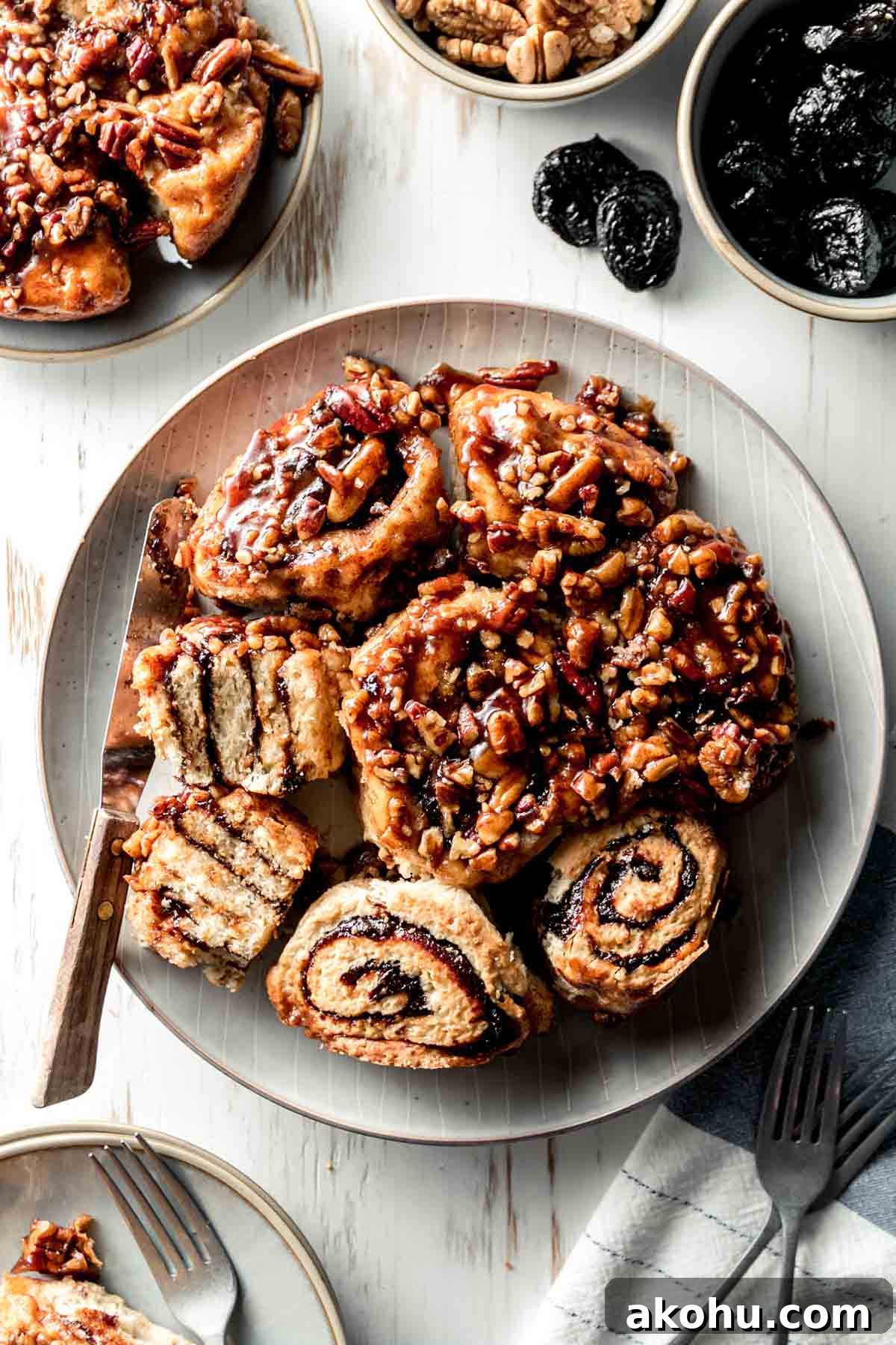 A plate full of gluten free sticky buns with gooey pecan caramel topping, some flipped over to show swirl of prune filling.