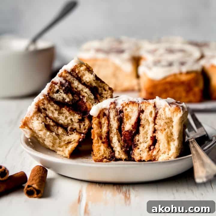 Cross section of a gluten free cinnamon roll on a plate with the rest of the rolls in the background.