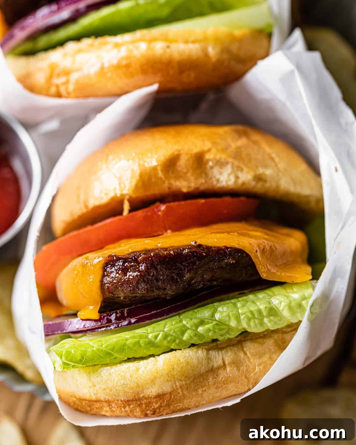 Up close image of burger with toppings wrapped in white paper.