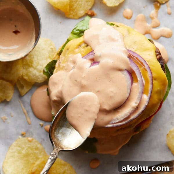 Gold spoon spreading burger sauce onto a burger.