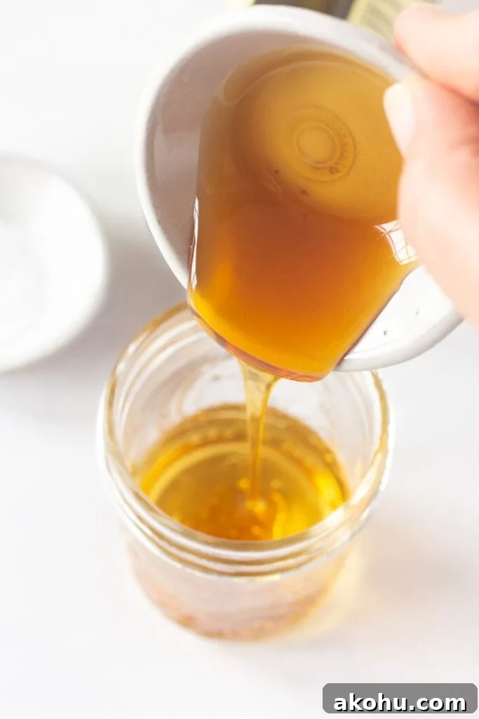 Close up of pouring honey from a small prep bowl into a mason jar with oil and vinegar already in it.