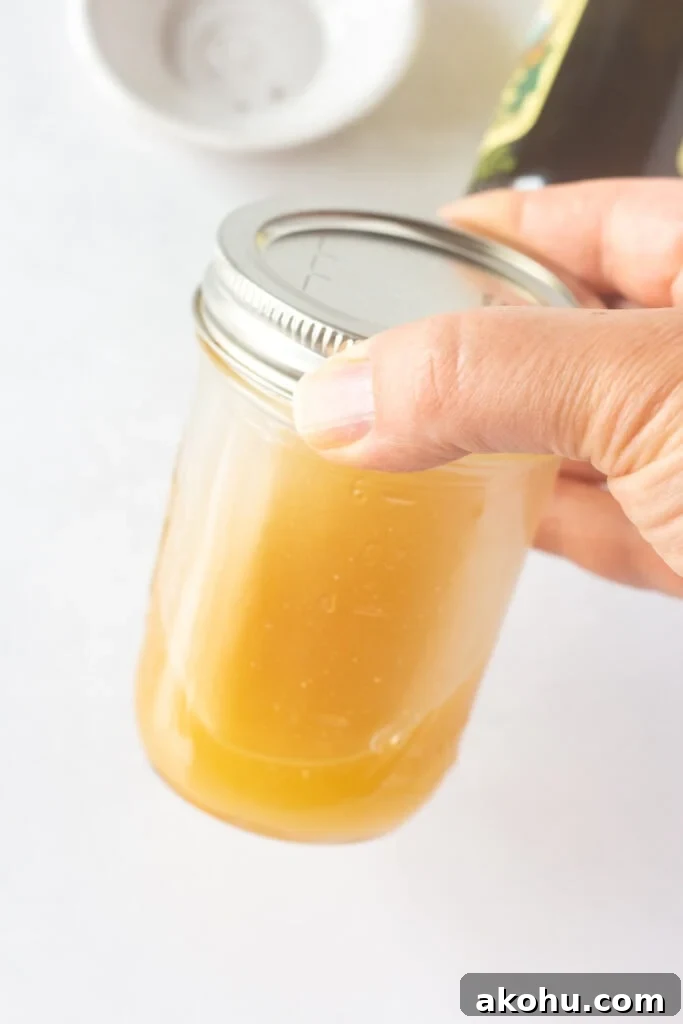 A hand shaking a small lidded mason jar with a gold-ish salad dressing in it.