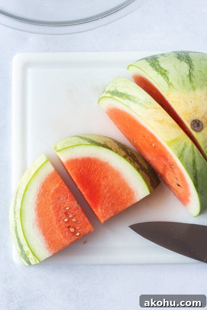 Top down shot of half a watermelon being sliced into quarters on a white cutting board.