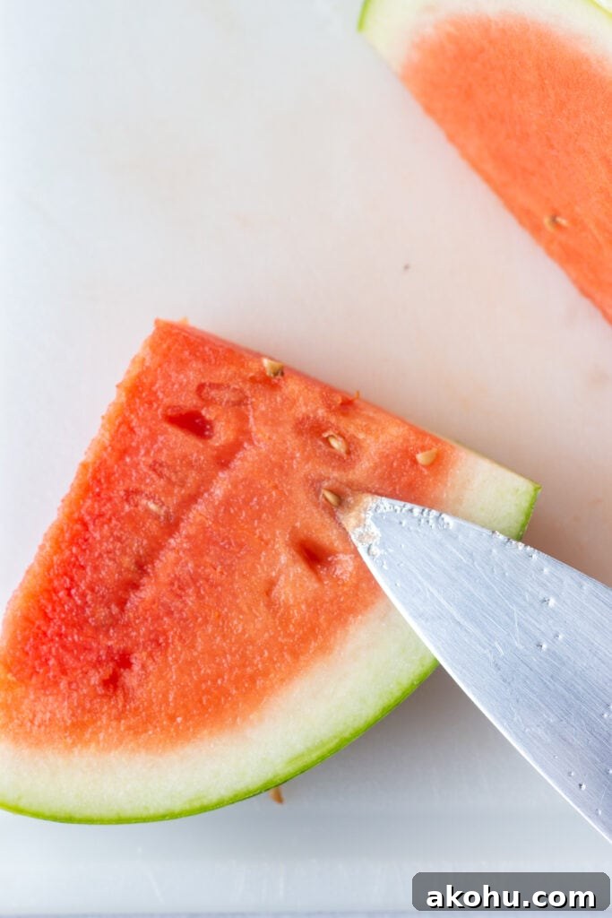 Close up of a sharp knife digging seeds out of a quartered slice of a watermelon.