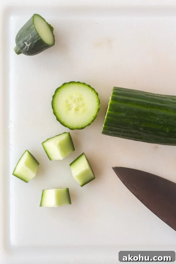 A cucumber being sliced and chopped into quarters on a white cutting board.