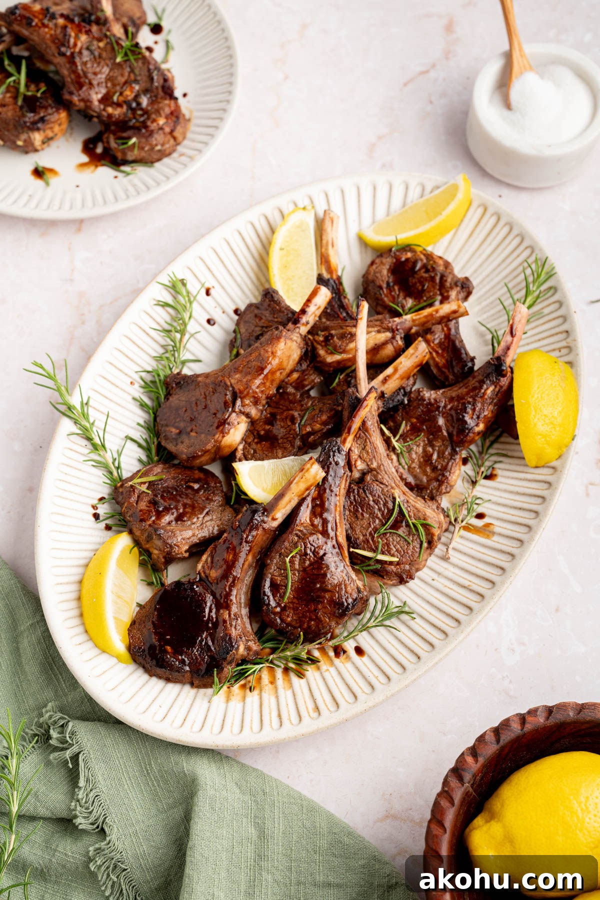 Balsamic-Glazed Oven Roasted Lamb Chops for Dinner 9 The baked lamb chops with balsamic honey glaze on a white serving plate garnished with rosemary and lemon wedges.