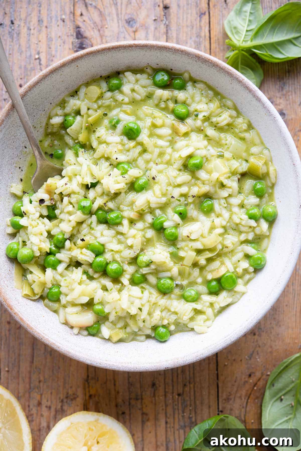 Creamy Pea and Basil Pesto Risotto 2 An overhead shot of a bowl of risotto made with peas and pesto on a wooden background with basil and lemons at the side