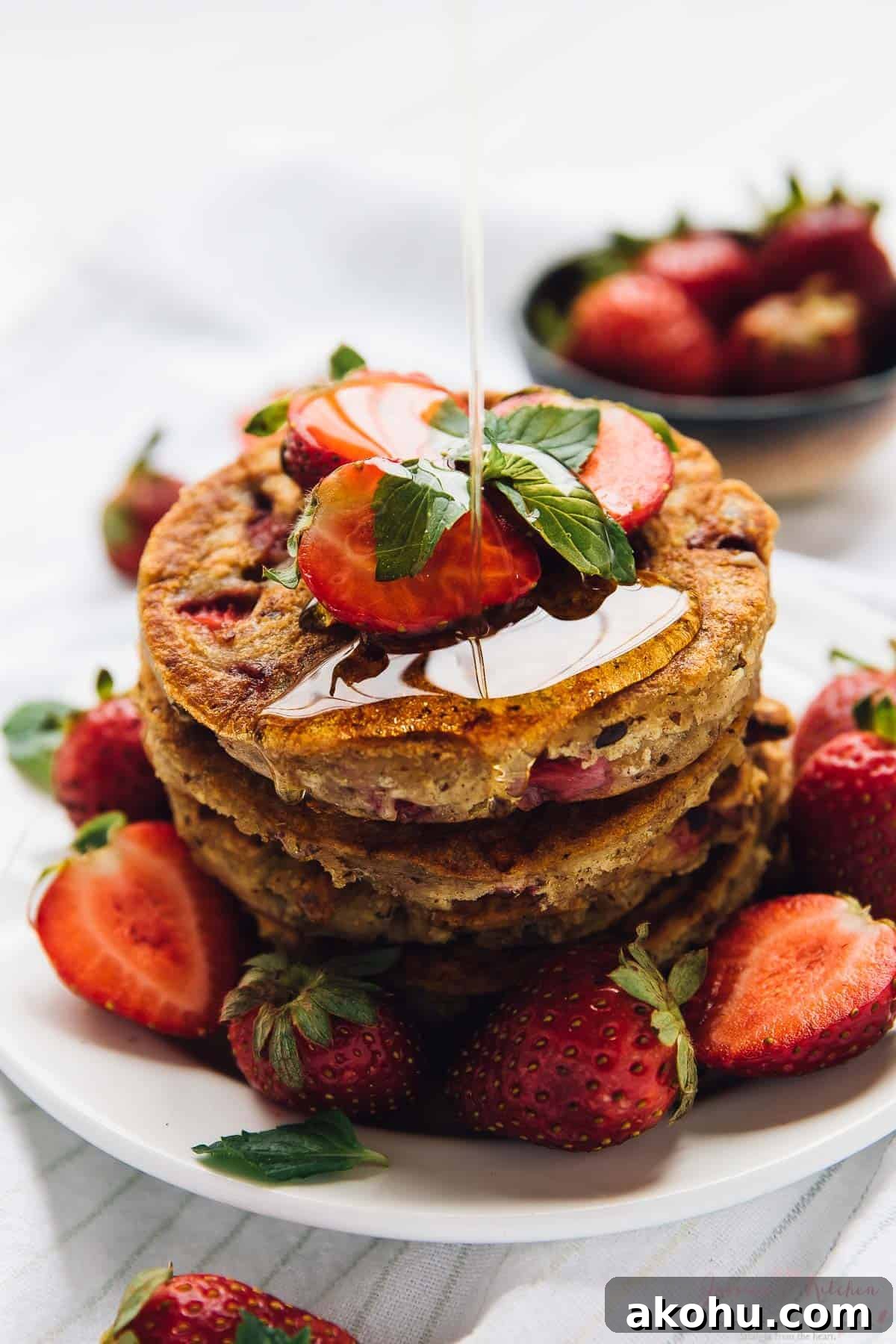 Strawberry pancakes—but make them gluten-free, plant-based, and PERFECTLY fluffy! Drizzling syrup onto stack of vegan gluten-free strawberry pancakes