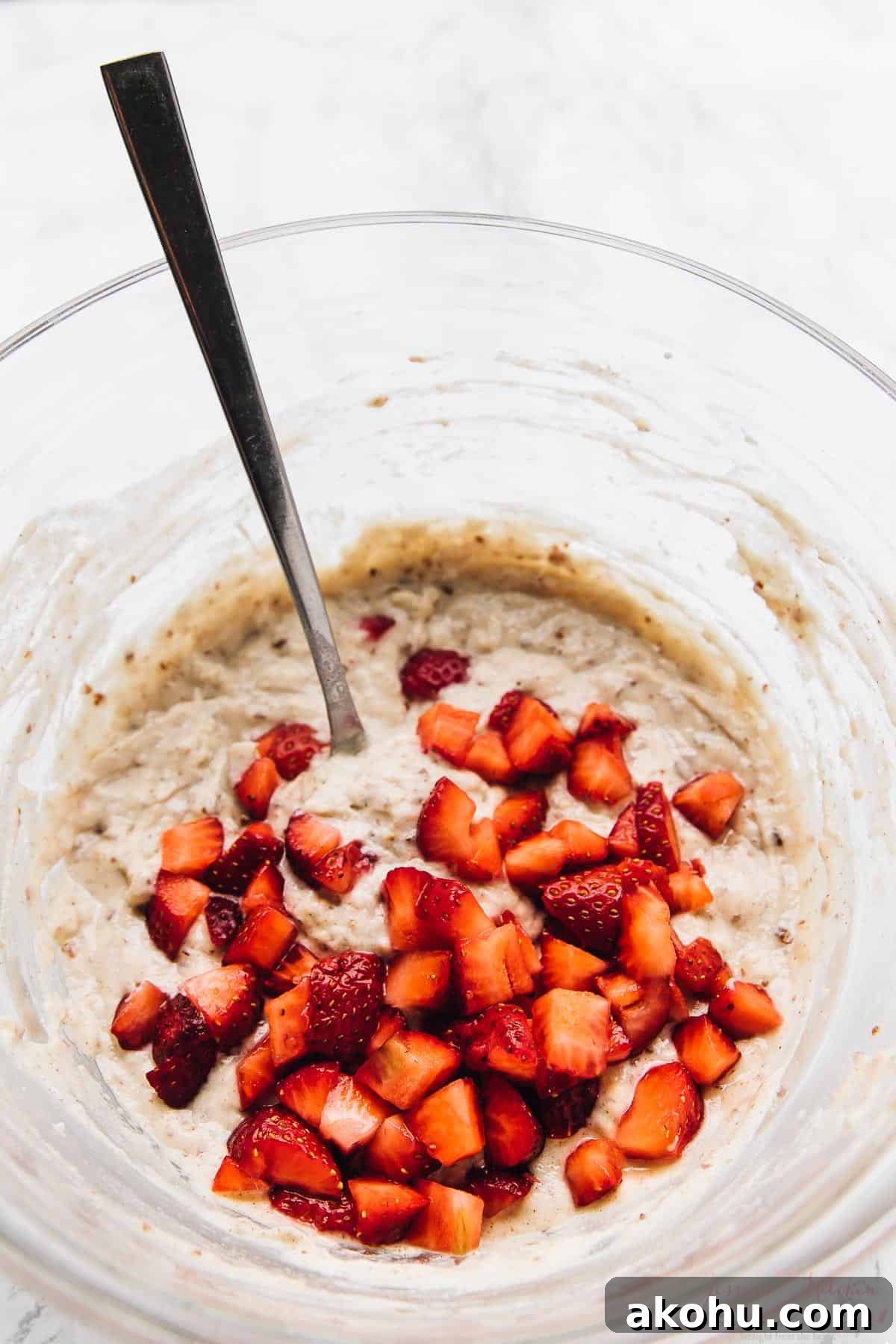 Strawberry pancakes—but make them gluten-free, plant-based, and PERFECTLY fluffy! Strawberries being stirred into pancake batter in glass mixing bowl