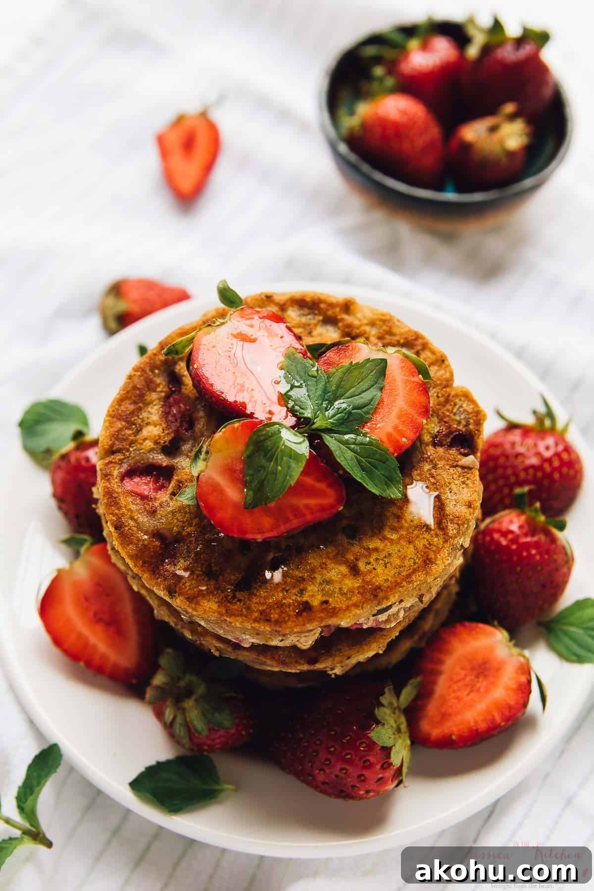 Strawberry pancakes—but make them gluten-free, plant-based, and PERFECTLY fluffy! Stack of strawberry pancakes on white plate, garnished with berries and syrup