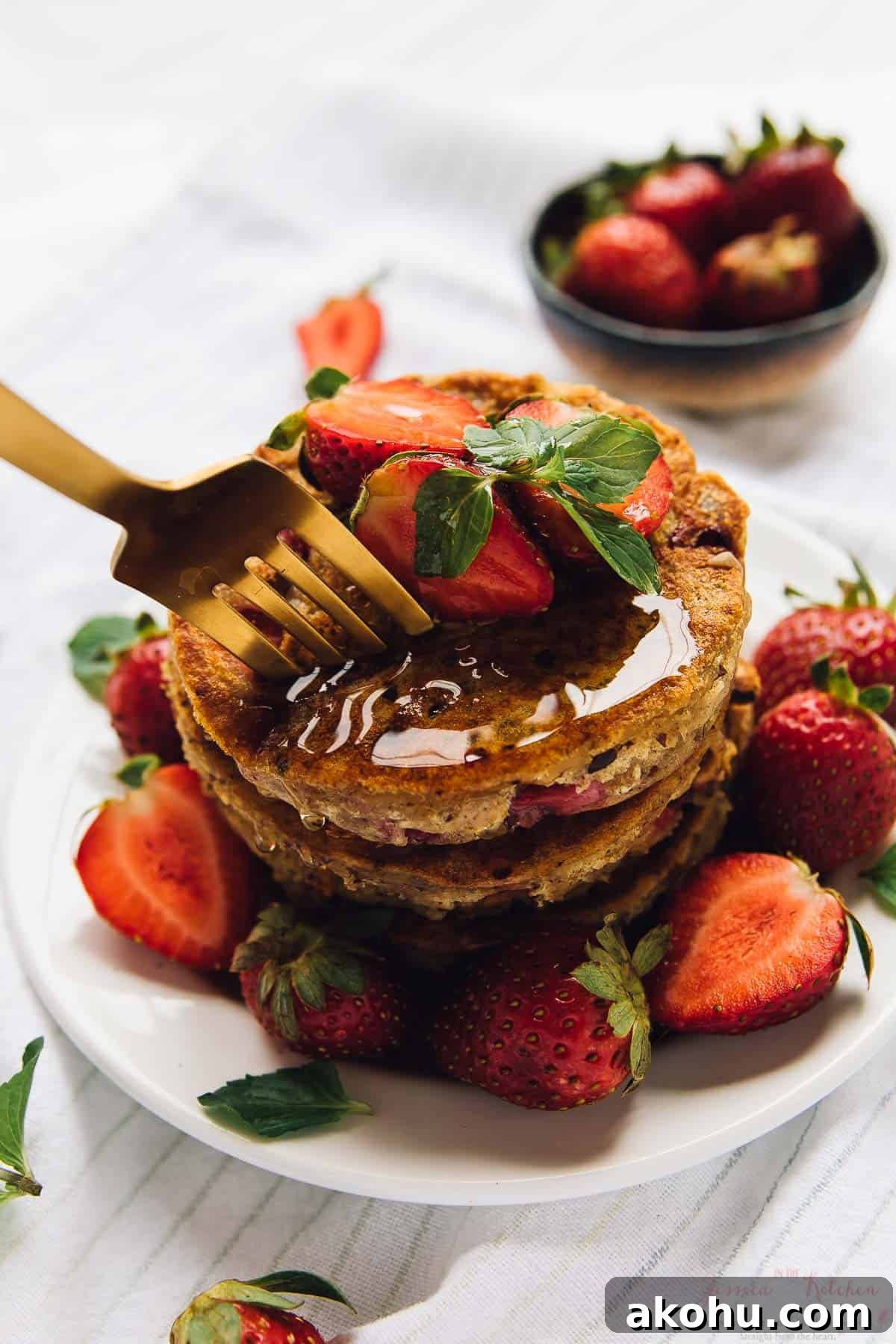 Strawberry pancakes—but make them gluten-free, plant-based, and PERFECTLY fluffy! Fork digging into stack of strawberry pancakes topped with syrup and berries