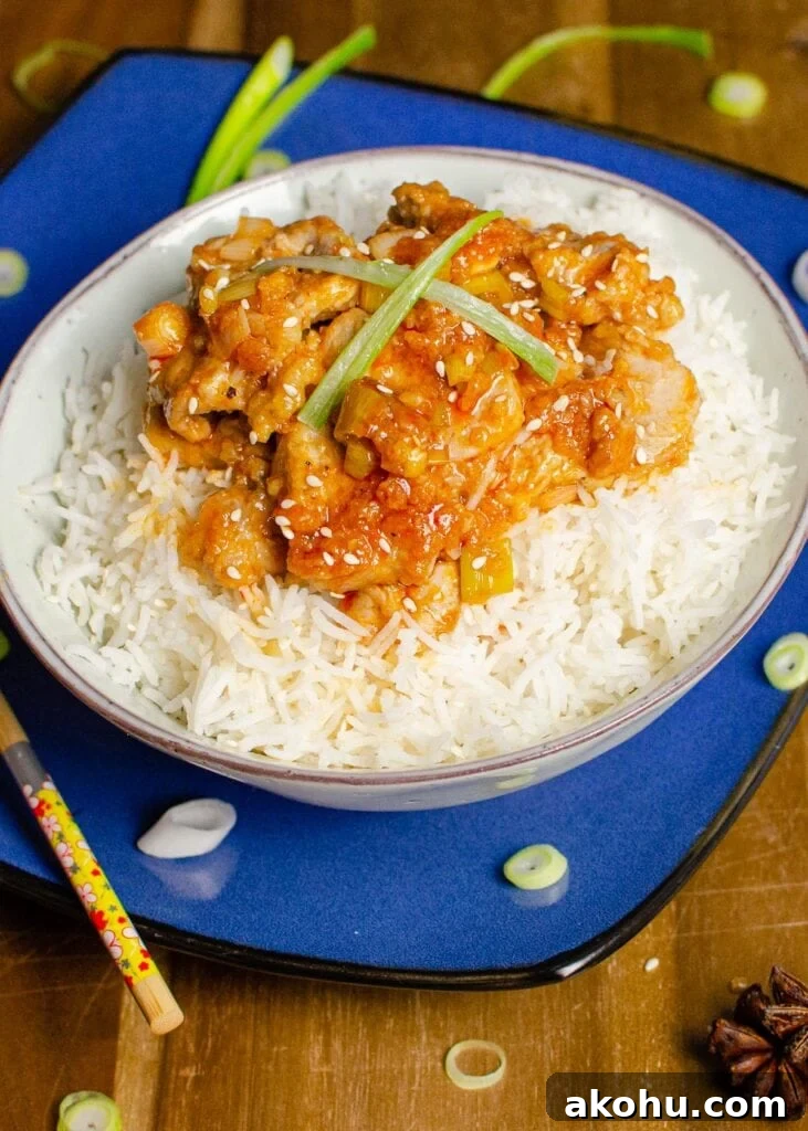 Hot and Spicy Pork served with rice in a green bowl on a blue plate with chopped spring onions on the sides