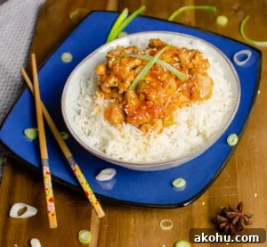 sizzling spicy pork served in a bowl with white rice on a blue plate with chopsticks,onions and star anise on the side