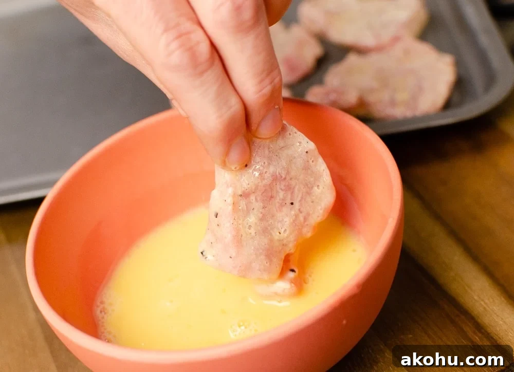 pork being dipped into whisked egg in an orange bowl to make our sizzling spicy pork