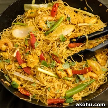 Singapore rice Noodles cooked in a wok with tongs on top