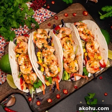 Four shrimp wraps filled with salad, king prawns and coated in sweet chilli sauce on a wooden chopping board with chopped red chillies around the tacos