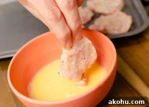 pork being dipped into whisked egg in an orange bowl to make our sizzling spicy pork