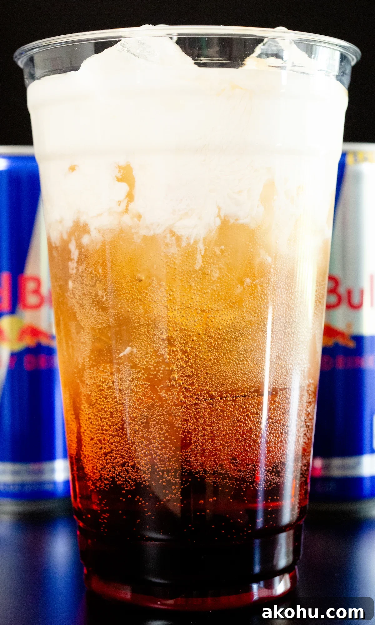 How to Make Sparkling Red Bull Italian Soda at Home 2 A large plastic glass filled with Red Bull Italian Soda. It has distinct layers of raspberry syrup, red bull soda, and cream on top.