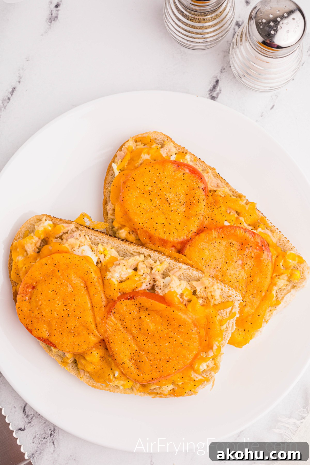 Crispy Air Fryer Tuna Melt Sandwich Recipe 11 Overhead shot of a tuna melt cooked In the air fryer, topped with tomatoes and melted cheese, and served on a round white plate.