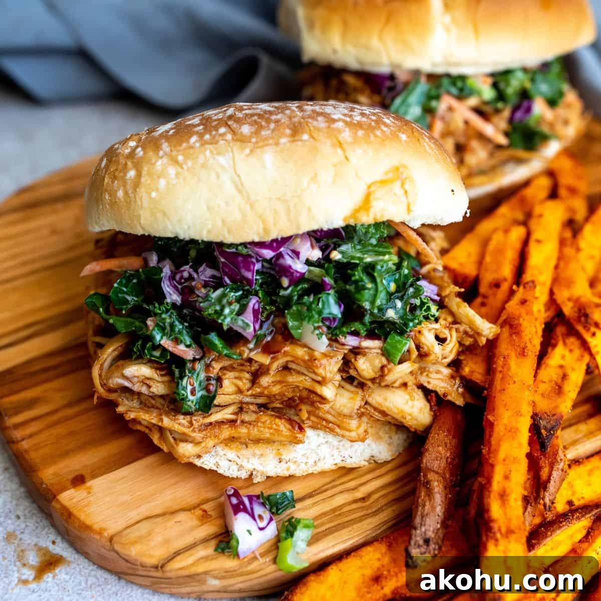 Pulled chicken sandwich on a cutting board  with a side of sweet potato fries.
