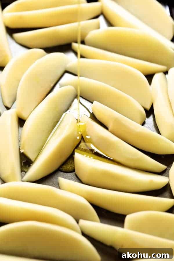 Photo of raw potatoes on baking sheet being drizzled with olive oil.