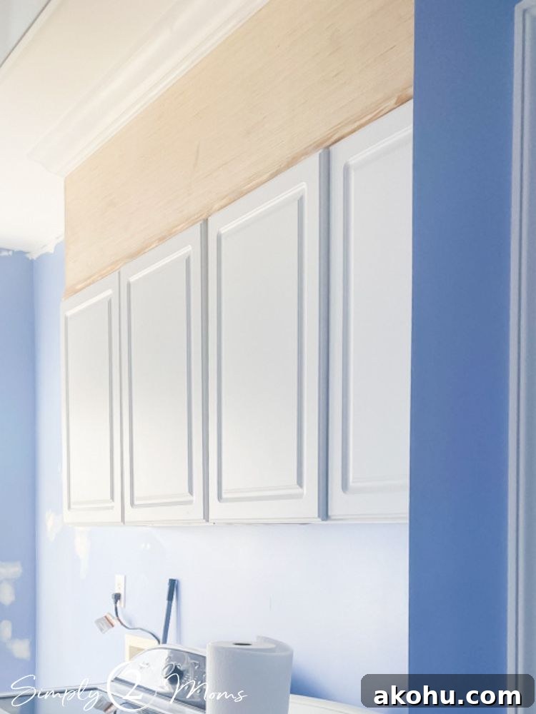 How to Close the Gap Above Kitchen Cabinets for a Finished Look 9 Set of four white cabinets with custom wooden topper and trim at ceiling height