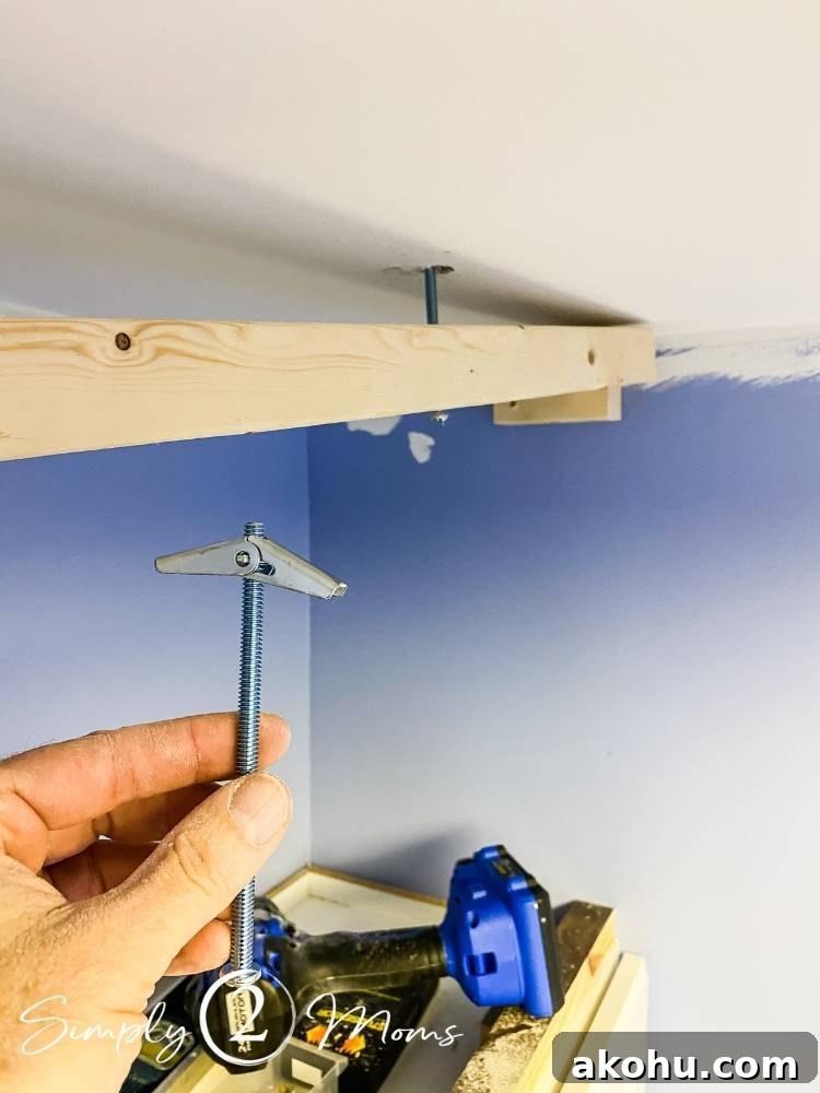 How to Close the Gap Above Kitchen Cabinets for a Finished Look 4 hand holding a toggle bolt to securely attach wood to drywall when there isn't a stud