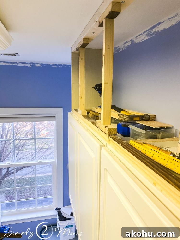 How to Close the Gap Above Kitchen Cabinets for a Finished Look 7 Cabinet topper construction process with one side enclosed and two wooden support beams in place between cabinet tops and ceiling