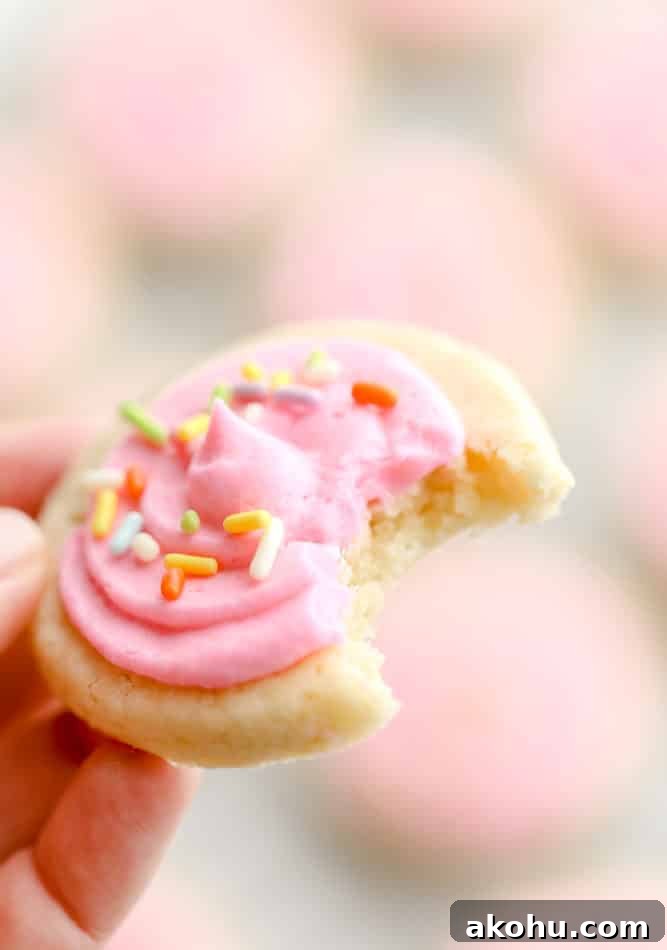 hand holding up a cookie with a bite taken out with pink frosting and sprinkles