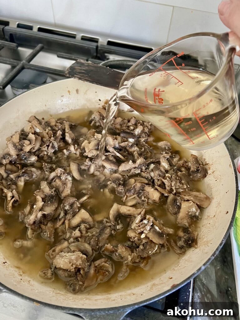 Pouring white wine into musrooms in pan.