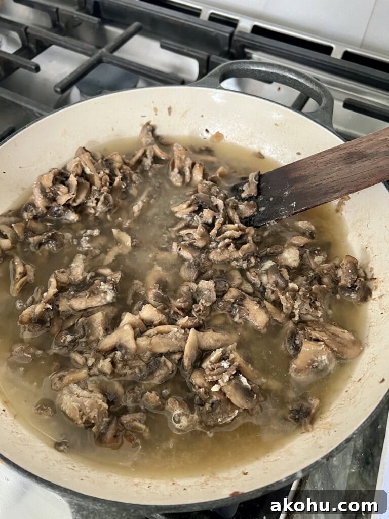 Mixing broth into mushrooms in pan.