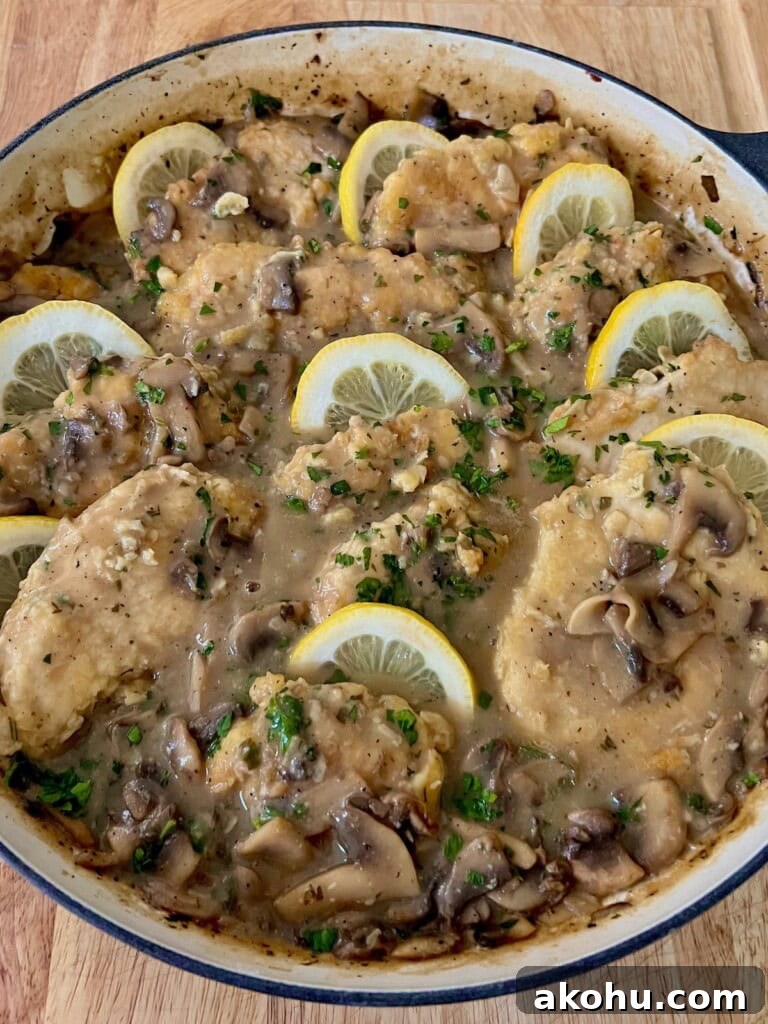 Finished Italian chicken francese with mushrooms in pan with lemon slices.