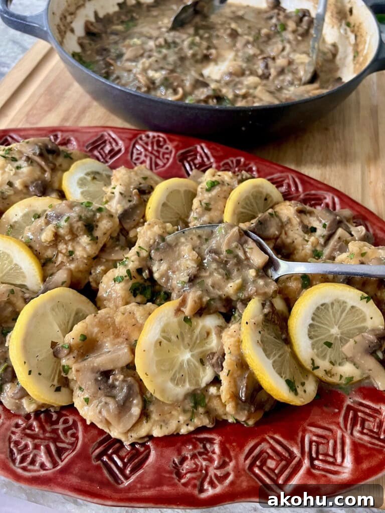 Italian Chicken and Mushrooms, Francese style, on red serving platter with lemon garnish and spoon of sauce.