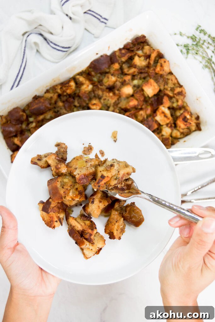 Pretzel and Sausage Stuffing with Beer for Holiday Dinners 3 A woman holds a white plate with a serving of sausage pretzel stuffing on it with a fork