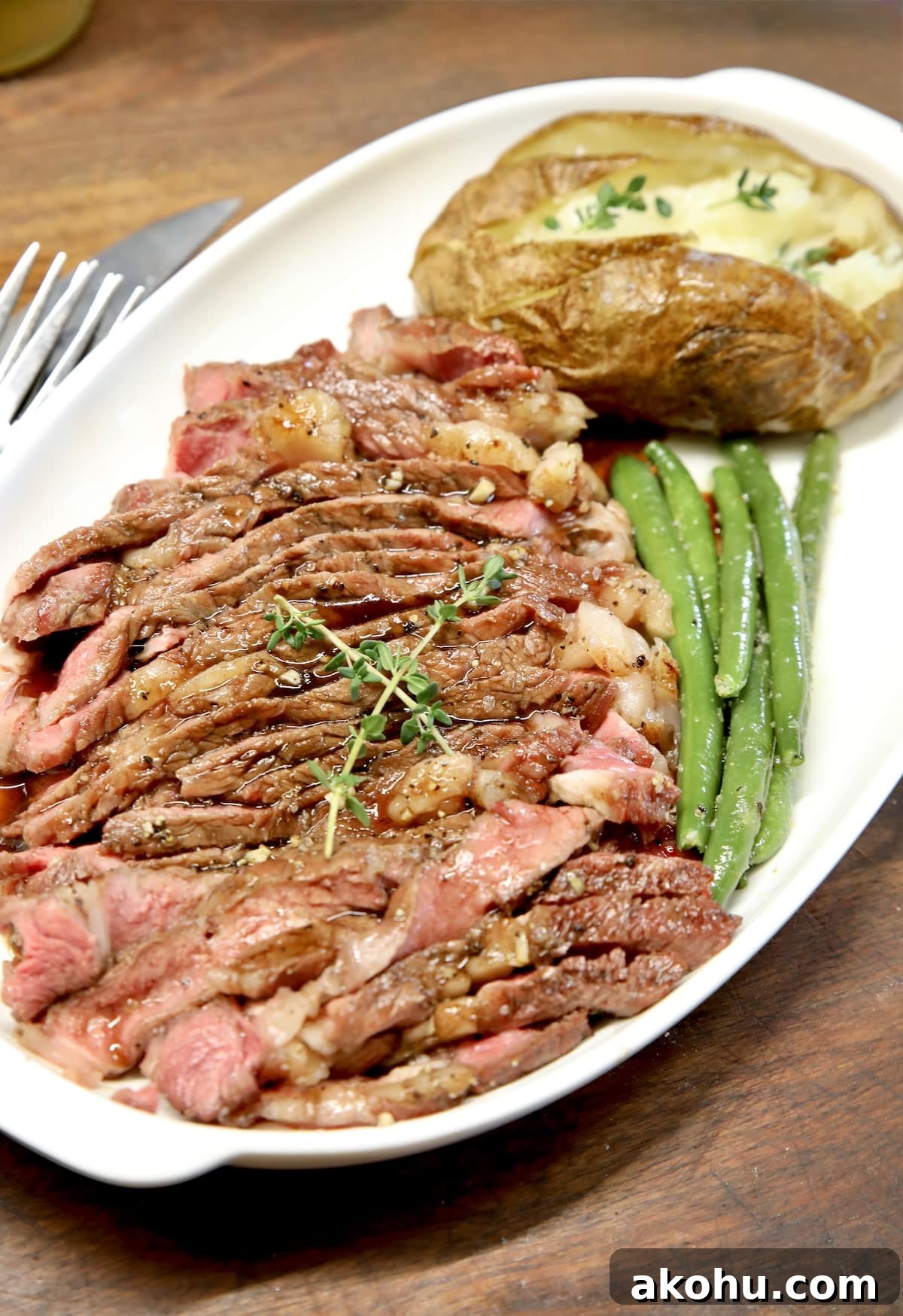 Glazed steak with baked potato and green beans. Platter with sliced steak, baked potato, green beans.