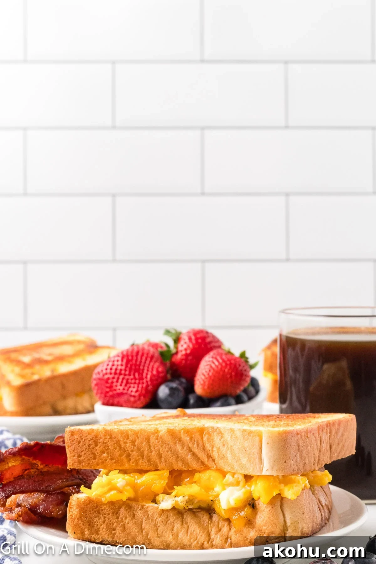 Fluffy Scrambled Egg Sandwich Recipe for Quick Breakfast 2 Scrambled Egg Sandwich on a plate with a side of bacon and a bowl of fresh fruit and coffee