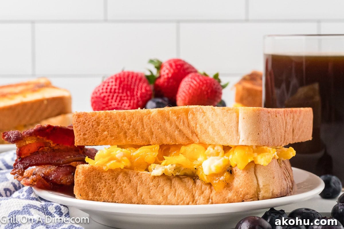 Fluffy Scrambled Egg Sandwich Recipe for Quick Breakfast 8 Scrambled Egg Sandwich on a plate with a side of bacon and a bowl of fresh fruit in the background